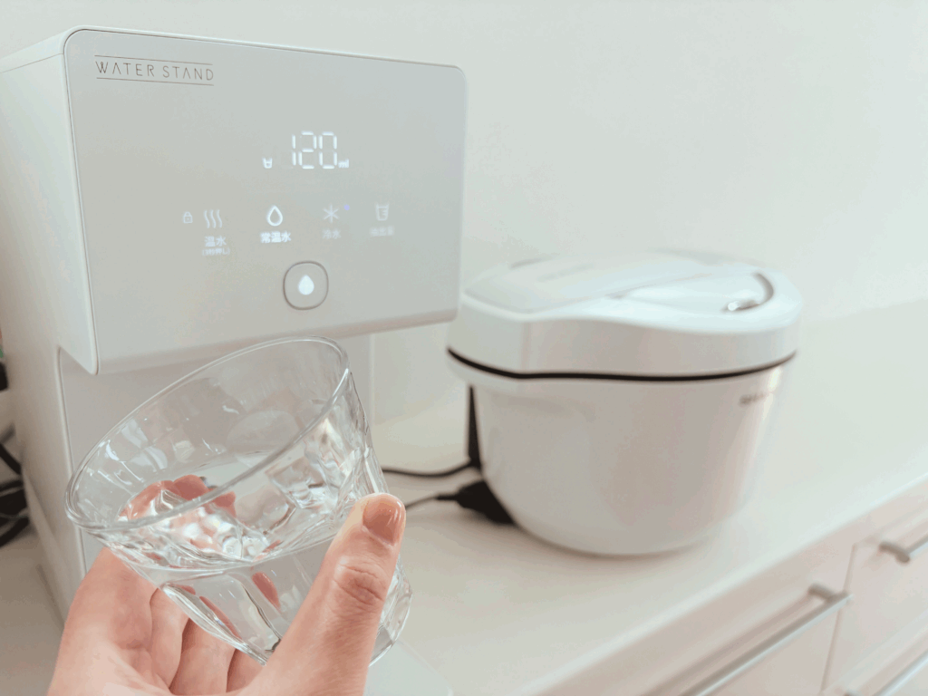 ウォータースタンドの本体の前で、水の入ったコップを持っている画像